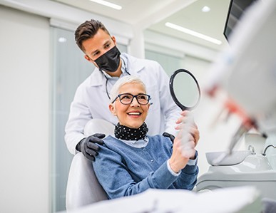 Patient smiling at reflection in handheld mirror with dentist