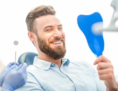 Man smiling into mirror after getting dental bridge in Superior