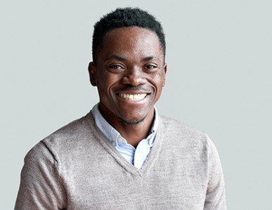 A young man wearing a gray V-neck sweater and showing off his healthy smile after seeing his Delta Dental dentist in Superior