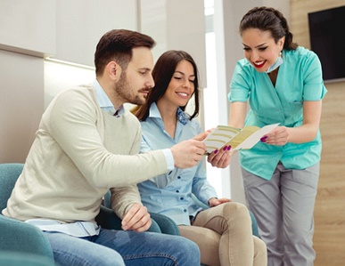 A couple seated in the waiting room and looking over a brochure while a dental receptionist discusses payment options