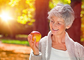 Woman with dental implants in Superior holding an apple