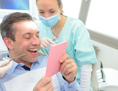 A male patient looking at his healthier smile after a dentist and hygienist complete periodontal therapy