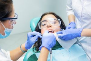 a female patient wearing protective eyewear while dentists perform a teeth cleaning