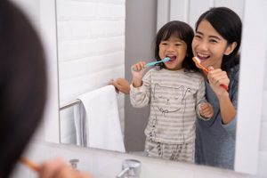 parent and a child brushing their teeth together in the bathroom