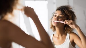 person brushing their teeth while looking in the mirror