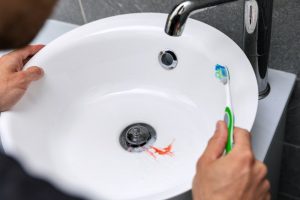 a person holding a toothbrush while blood sits in the sink because of bleeding gums