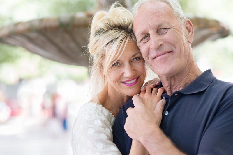 a middle-aged man and woman hugging and smiling after receiving dental implants in Superior