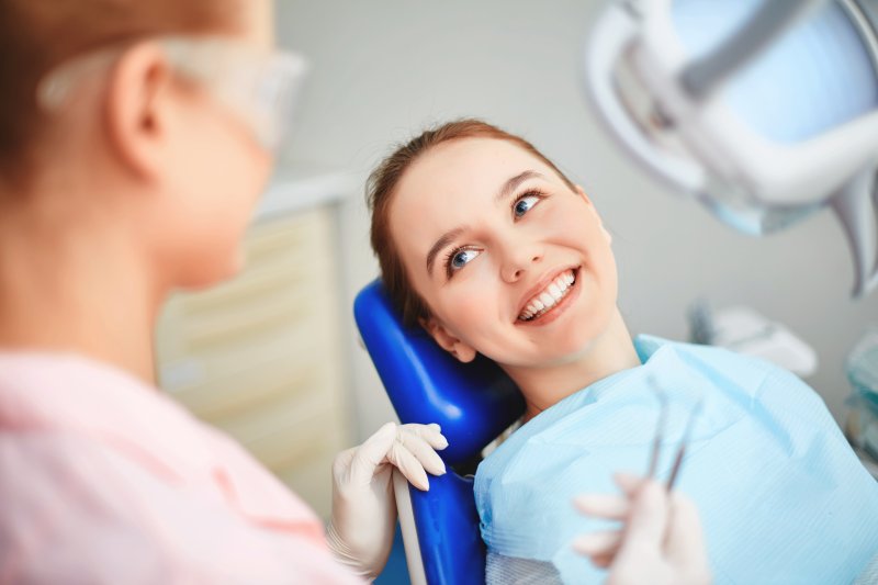 Young woman laying in dental chair smiling up at dentist