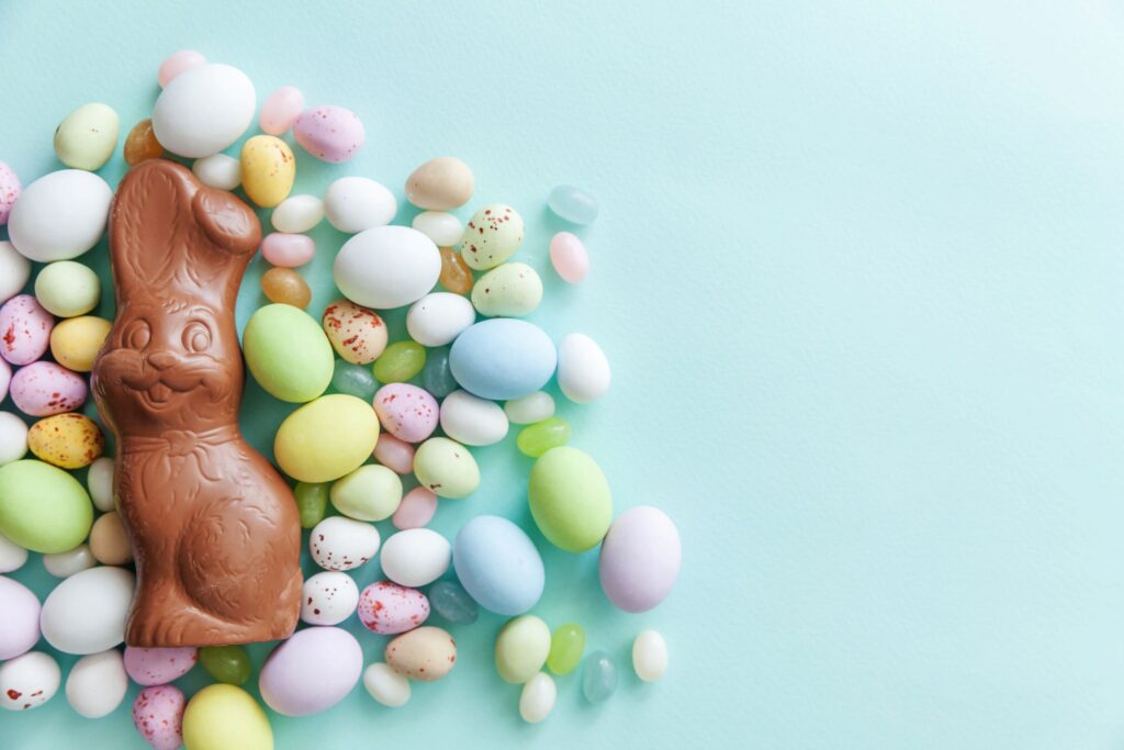 Chocolate bunny and egg-shaped candies on light blue surface