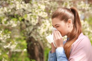 Woman blowing her nose with trees in background.